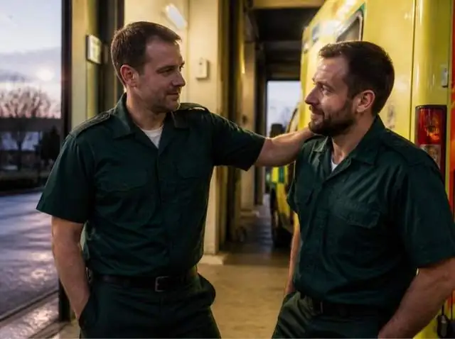 Two paramedics in green uniforms talking supportively beside an ambulance